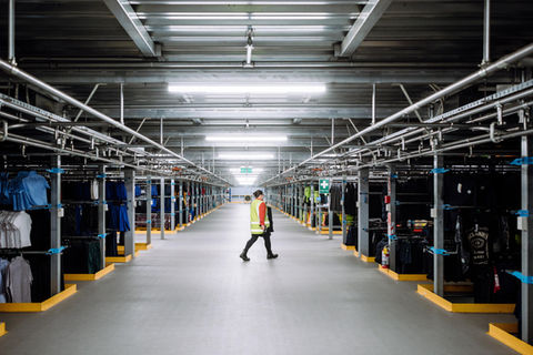 Warehouse worker walking down aisle with clothing racks; Distribution Centre – Overview.