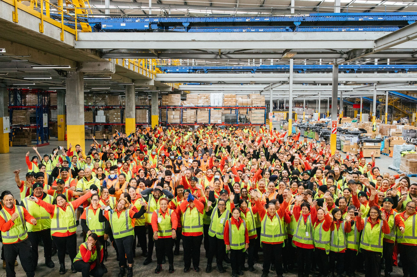 Large group of warehouse staff in high-visibility vests posing for photo