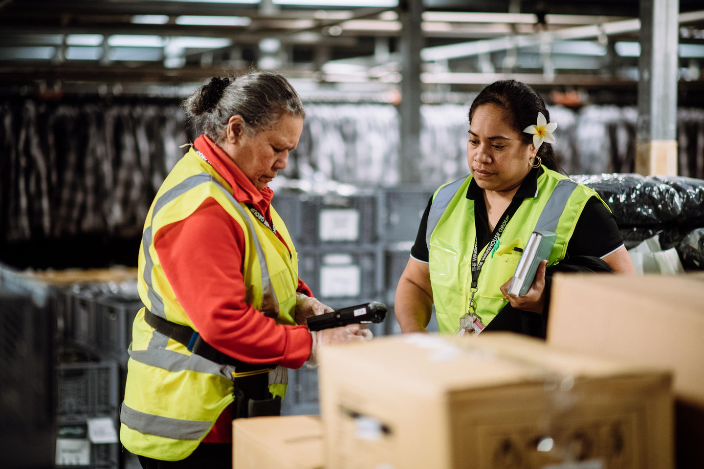 Two women wearing vests scan boxes in a distribution center for logistics jobs