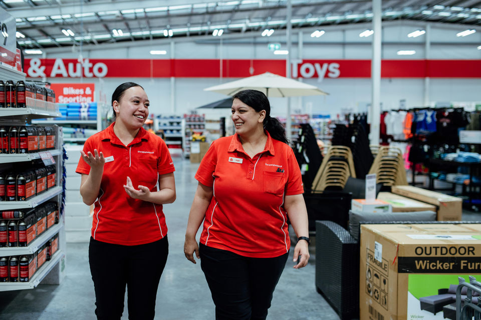 Two retail workers in red shirts walking through the store, Bikes & Auto, Toys.