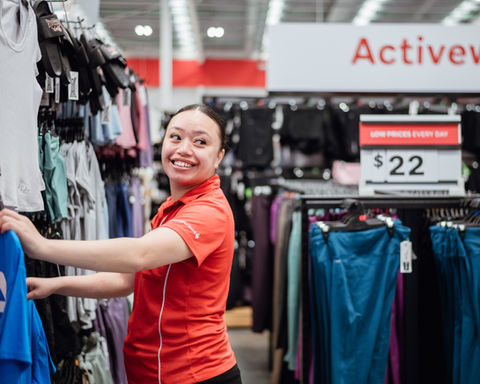 Smiling employee arranging clothes near Activewear sign and price tag $22.